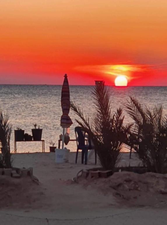 a sunset on the beach with a chair and an umbrella at Villa in Ouled Yaneg in Ouled Yaneg