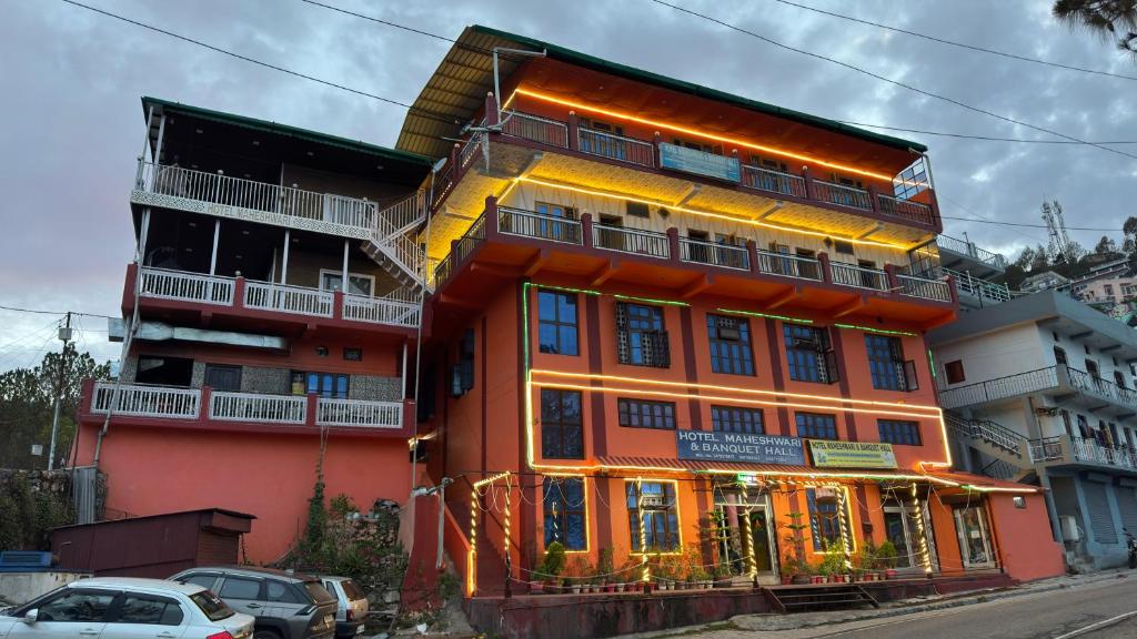 a tall orange building with cars parked in front of it at Hotel Maheshwari Tehri in Tehri-Garhwāl