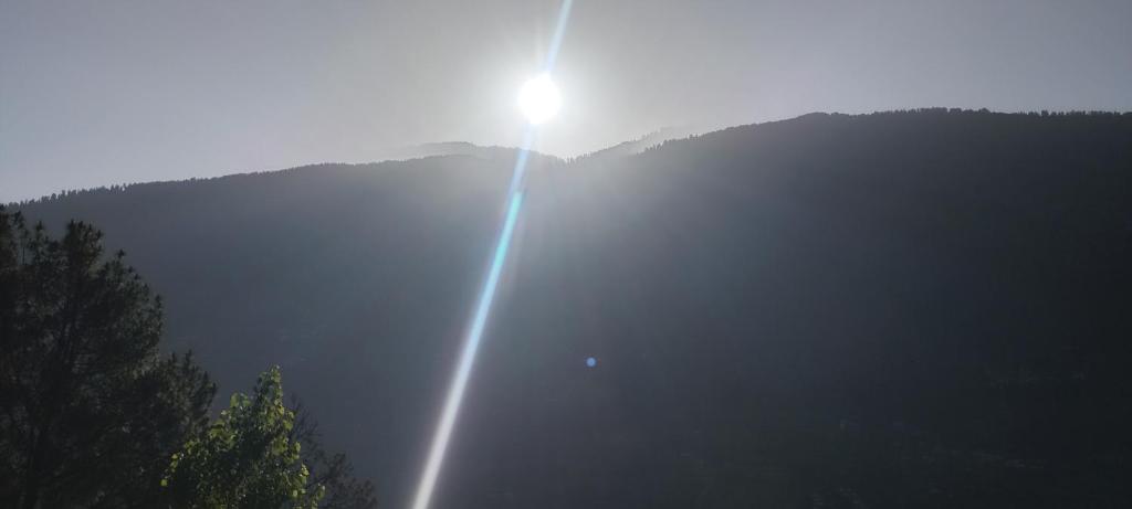 a sun is shining on a mountain with trees at Nothing in Kulu