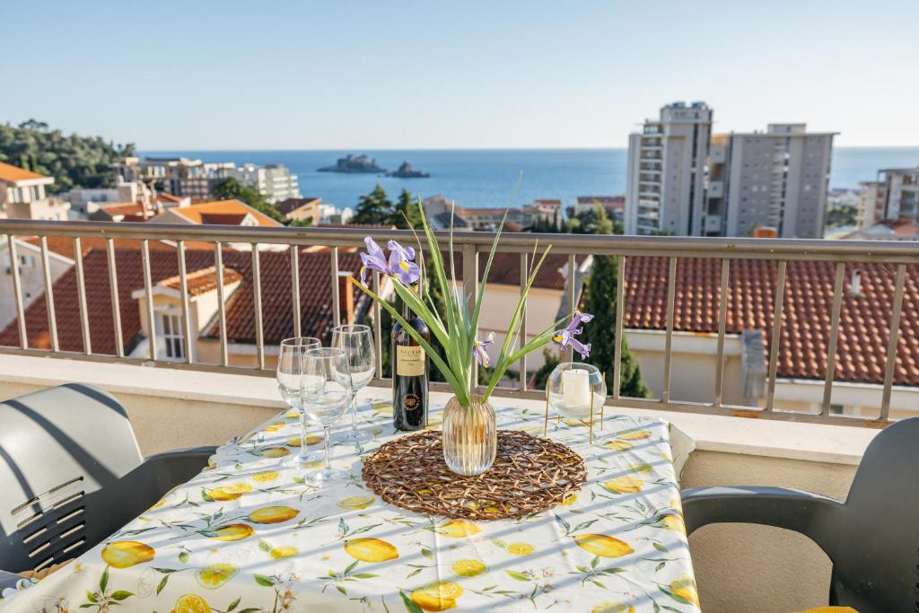 a table with wine glasses and flowers on a balcony at Apartments Nada in Petrovac na Moru