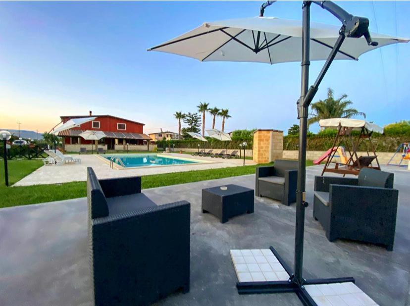 a patio with an umbrella and couches and a pool at Villa Stefy in Avola
