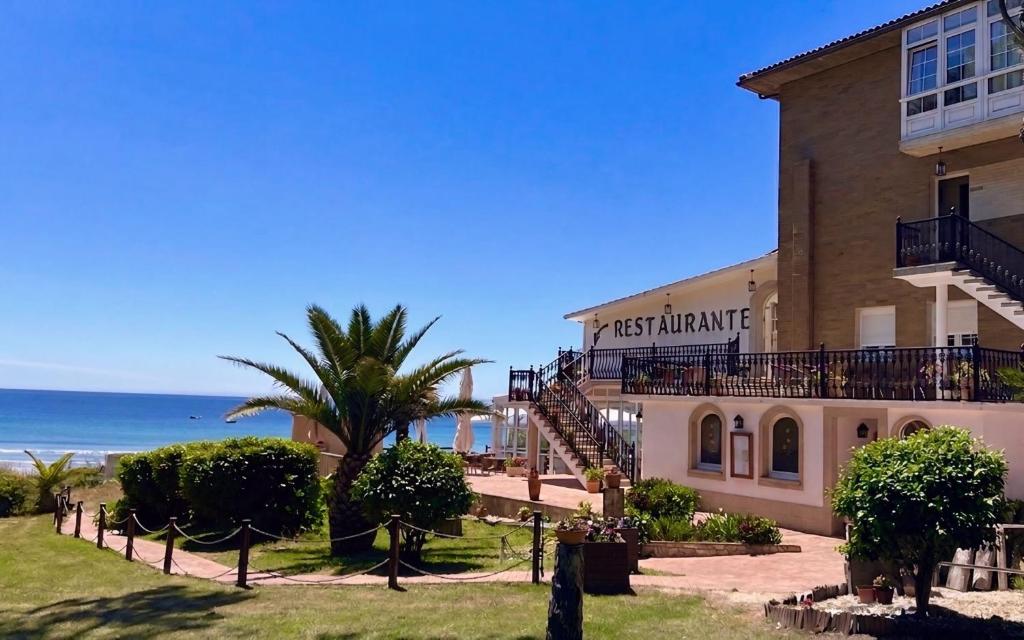 a building on the beach with the ocean in the background at Hotel Restaurante Playa de Estorde in Cee