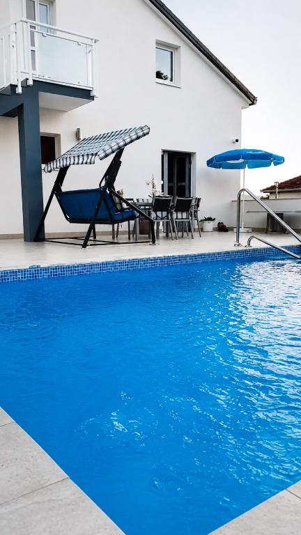 a blue swimming pool with chairs and umbrellas next to a house at Apartmani Novak in Mostar