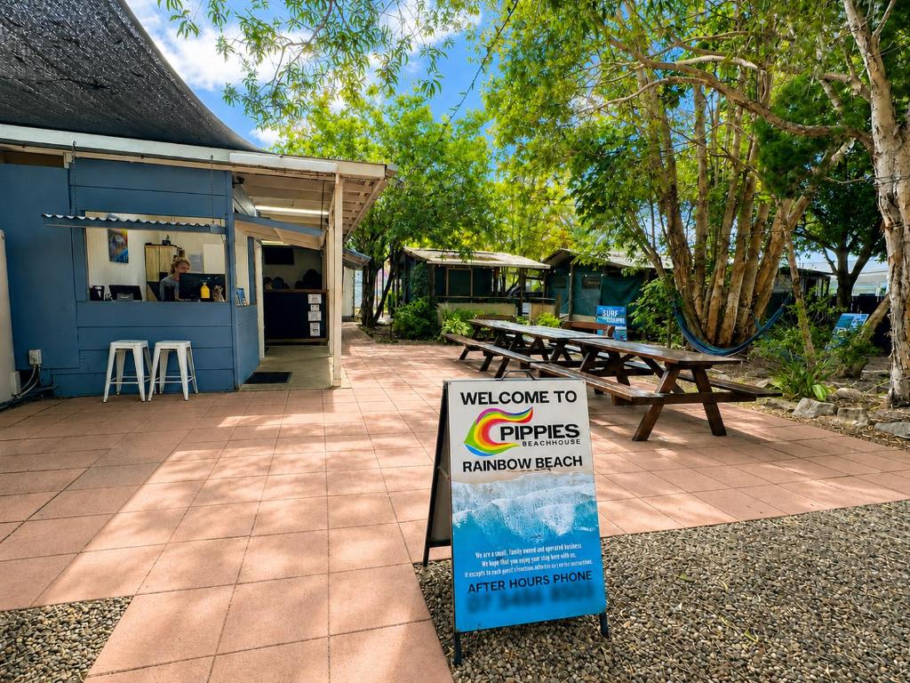 a sign in front of a building with a picnic table at Pippies Beachhouse Backpackers in Rainbow Beach