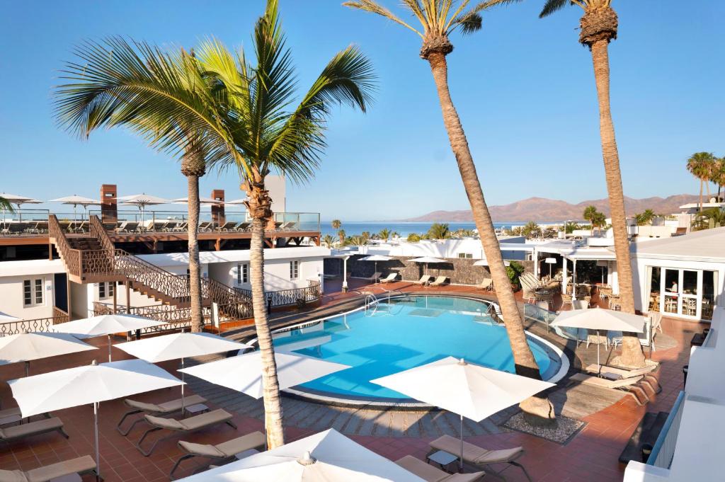 a swimming pool with palm trees and umbrellas at Plus Fariones Apartamentos in Puerto del Carmen