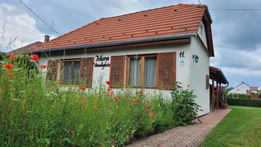 a white house with a red roof and a field of flowers at Mura Vendégház in Murakeresztúr