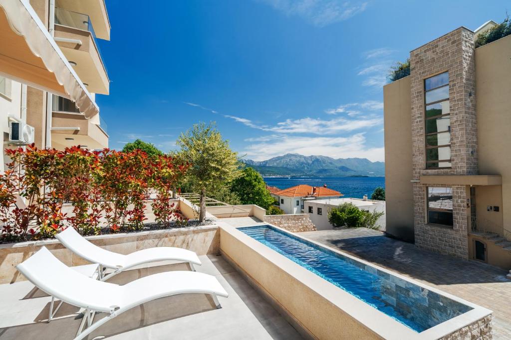 a balcony with a swimming pool and two white chairs at Boho Apartment with Sea View & Pool in Baošići