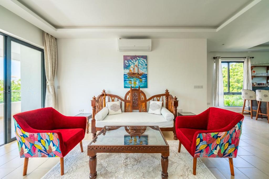 a living room with two red chairs and a white couch at Sandbox Apartment 4 Diani Beach Kenya in Ukunda