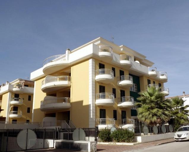 a large yellow building with balconies and palm trees at Il Ventaglio Apartment in Martinsicuro