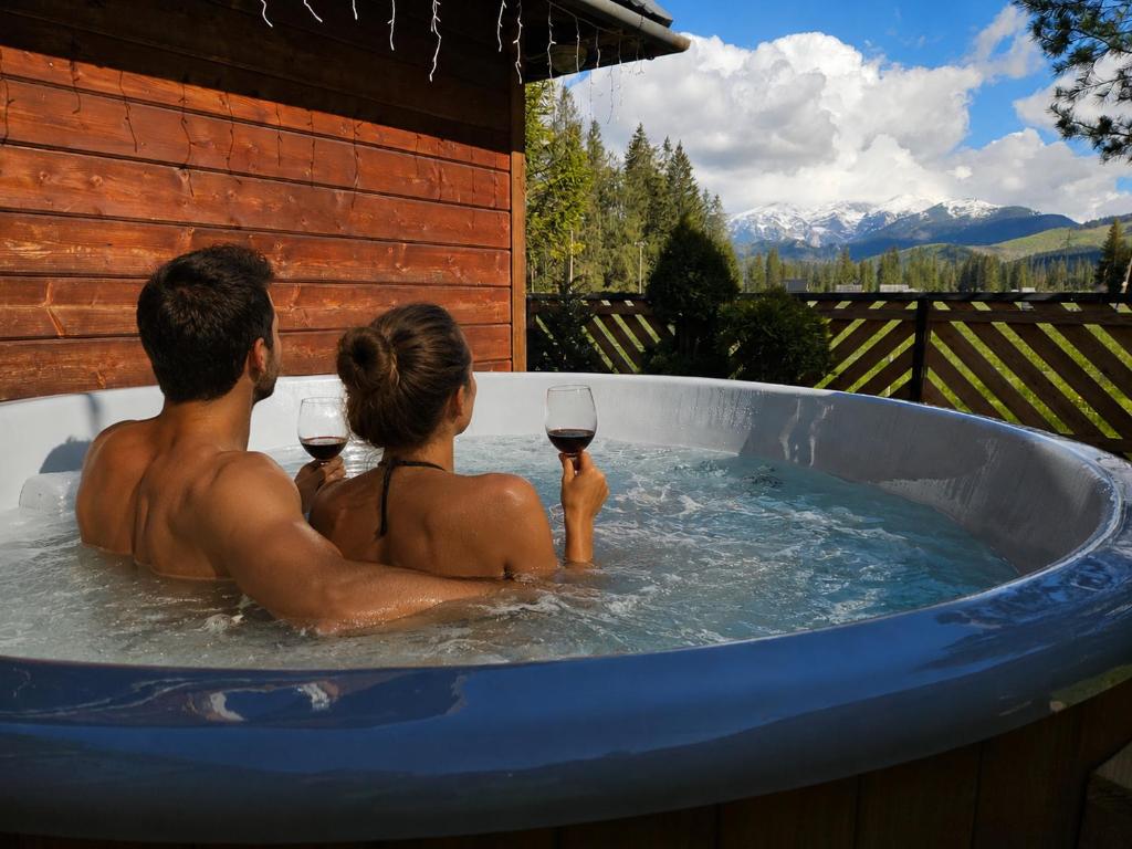 a man and woman sitting in a tub with glasses of wine at Domek drewniany Krokus in Witów