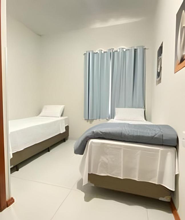 two beds in a white room with a window at Pousada Âncora - 14 Suítes completas com Ar, TV, Frigobar e Wi-Fi, para grupos ou viajantes individuais. in Gravataí