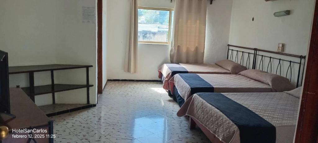 a hotel room with three beds and a window at Hotel San Carlos in Tizimín