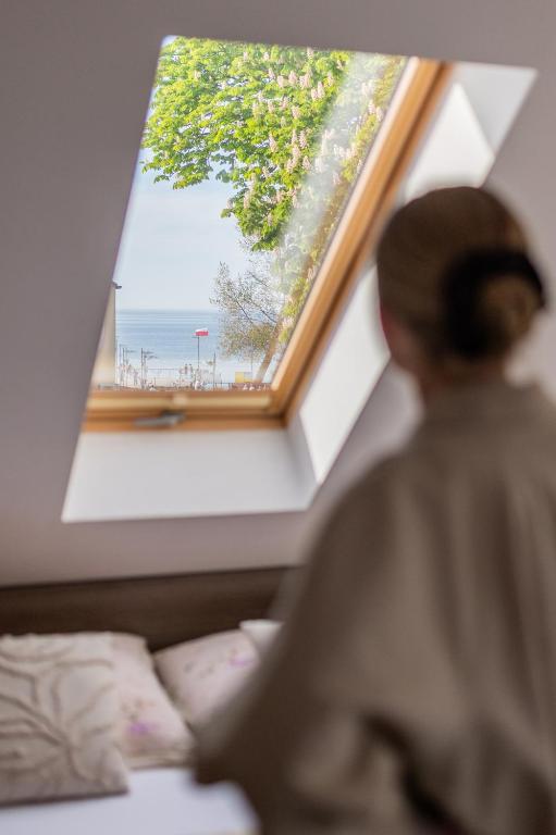 a woman sitting on a bed looking at a window at DOM GOŚCINNY ROMA in Rewal