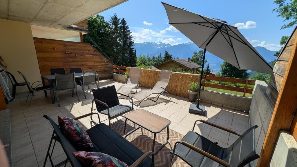 a patio with chairs and a table and an umbrella at Le Cormier - Appartement 6 personnes in Ovronnaz