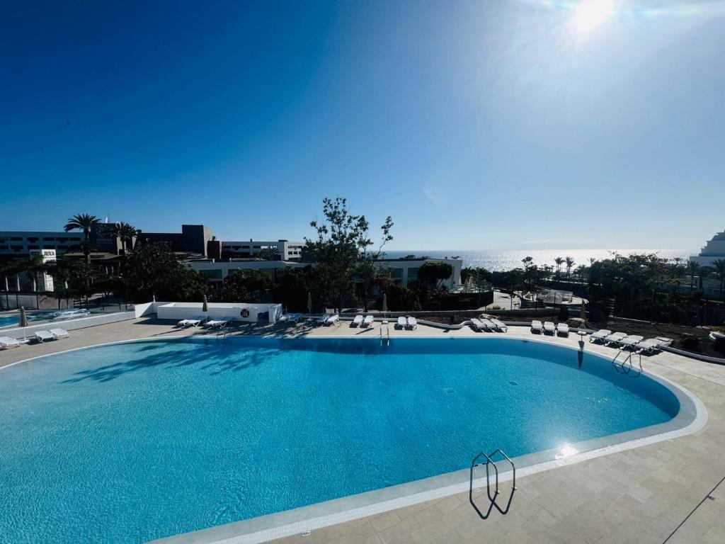 a large swimming pool with lounge chairs and the ocean at KAI Apartment Playa Paraiso in Playa Paraiso
