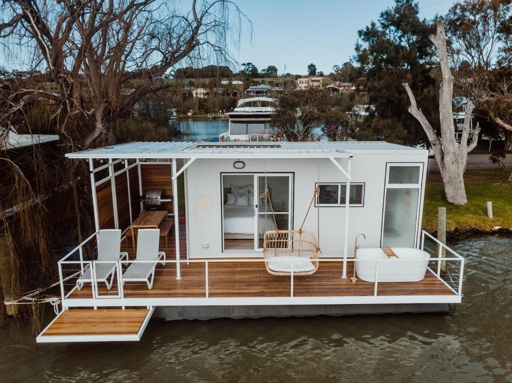 a small white boat on the water with chairs at The Floathouse - Floating tiny home on the Murray in White Sands
