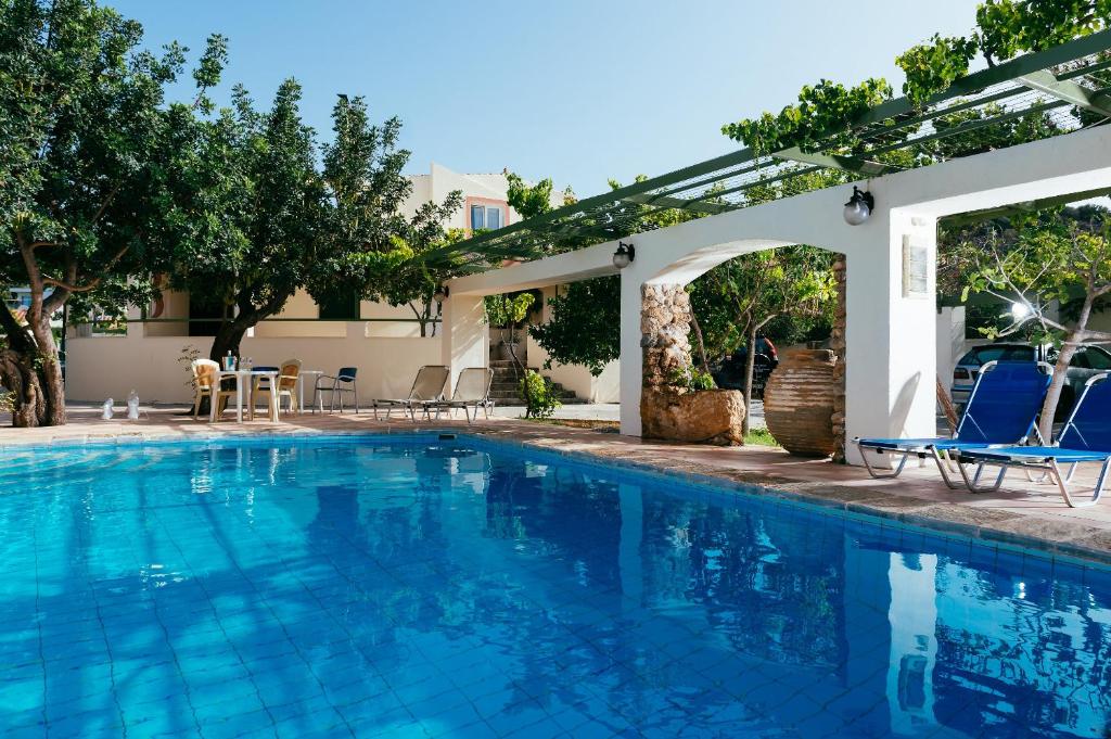 una piscina con sillas azules y pérgola en Ammoudara Beach Hotel Apartments, en Agios Nikolaos