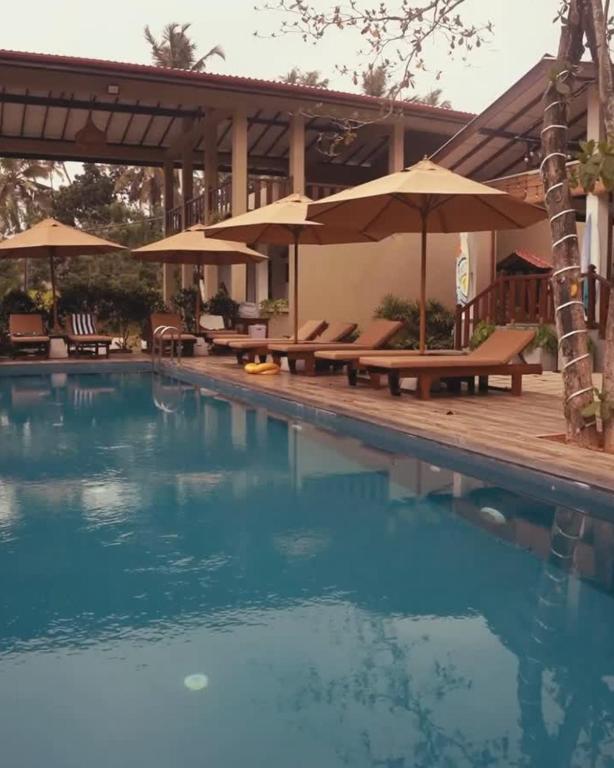 a swimming pool with benches and umbrellas at NatureSurf Villas - Private Garden Retreat at Hiriketiya Beach SPA, Surf & Relaxation in Dickwella