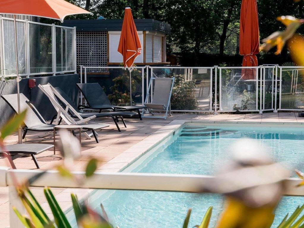 a swimming pool with chairs and umbrellas next to it at Novotel Orléans Chemins De Sologne Demeures De Campagne in Orléans