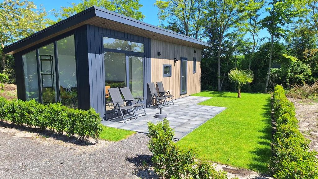 a small house with glass doors and chairs in a yard at B&B ZomersBuiten in Oude Pekela