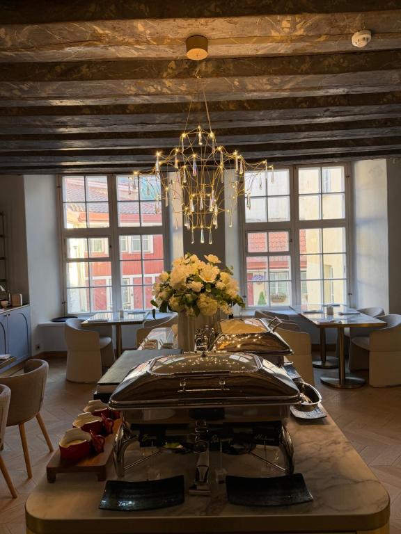 Breakfast buffet with chafing dishes, white floral centerpiece and crystal chandelier by large windows with red-tiled roofs at The Three Sisters Hotel in Tallinn
