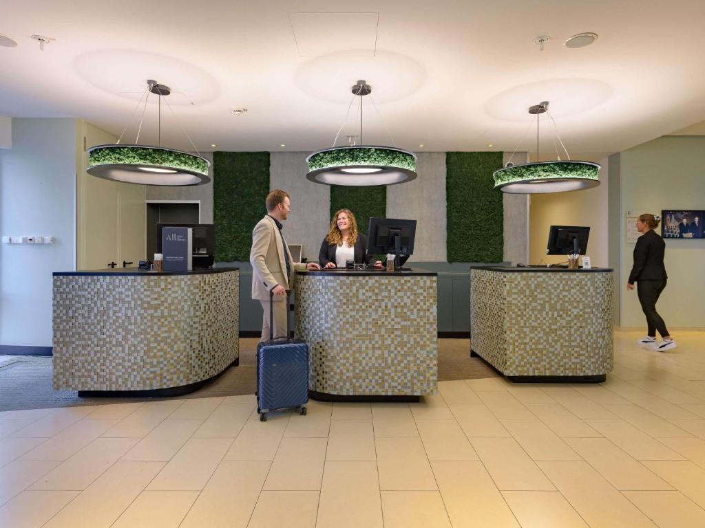 a man and woman waiting at a counter in a lobby at Mercure Hotel Köln West in Cologne
