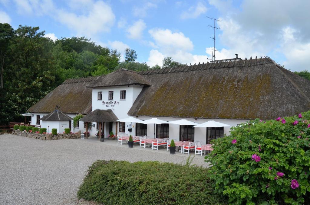 a white building with a thatched roof with tables and chairs at Bromølle Kro in Jyderup