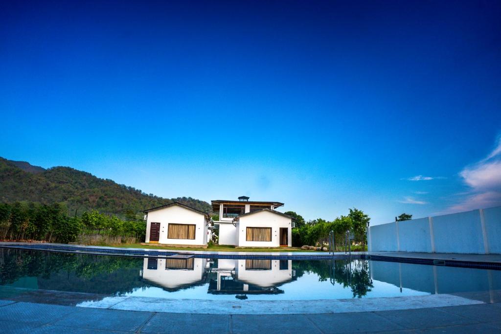 a house is reflected in the water of a swimming pool at Corbett Retreat in Rāmnagar