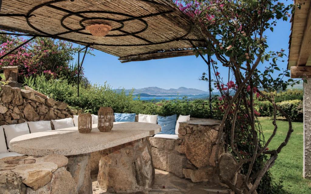 a stone table and chairs under a pergola at Amazing Two-Bedroom House with Sea View in Cala di Volpe in Porto Cervo