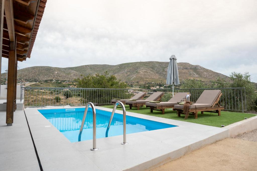 a pool with chairs and an umbrella and mountains in the background at Lagonisi Olive Retreat in Kalívia Thorikoú