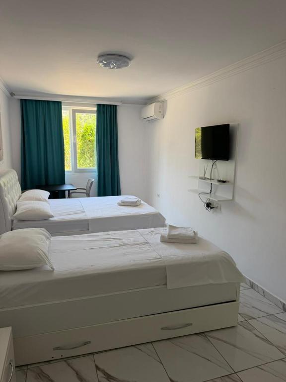 a white bedroom with two beds and a television at Elois Apartments in Shëngjin