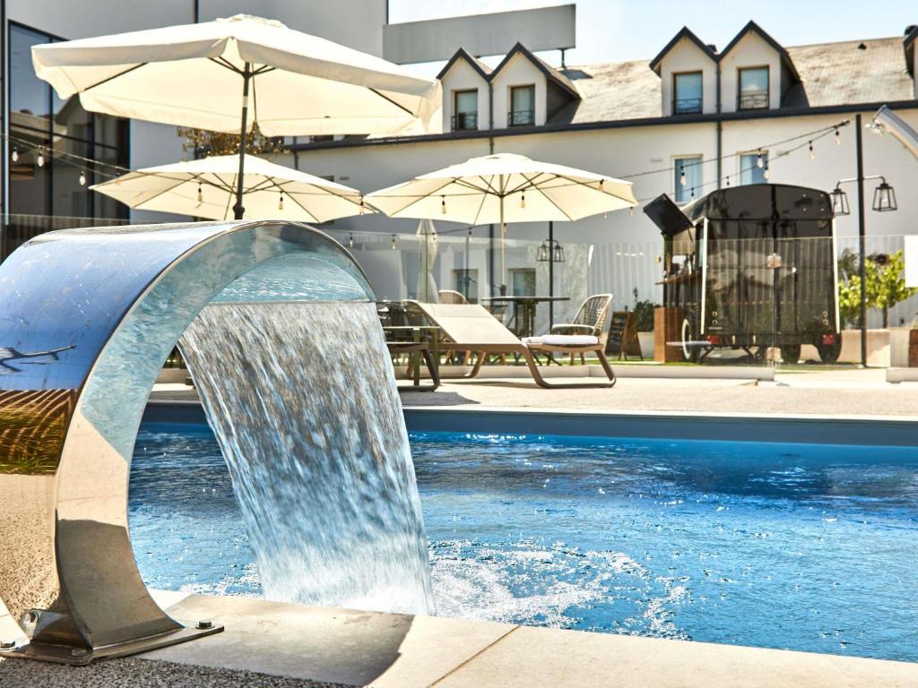 a water fountain in a pool with umbrellas at ibis La Roche Sur Yon Vendespace in Mouilleron-le-Captif