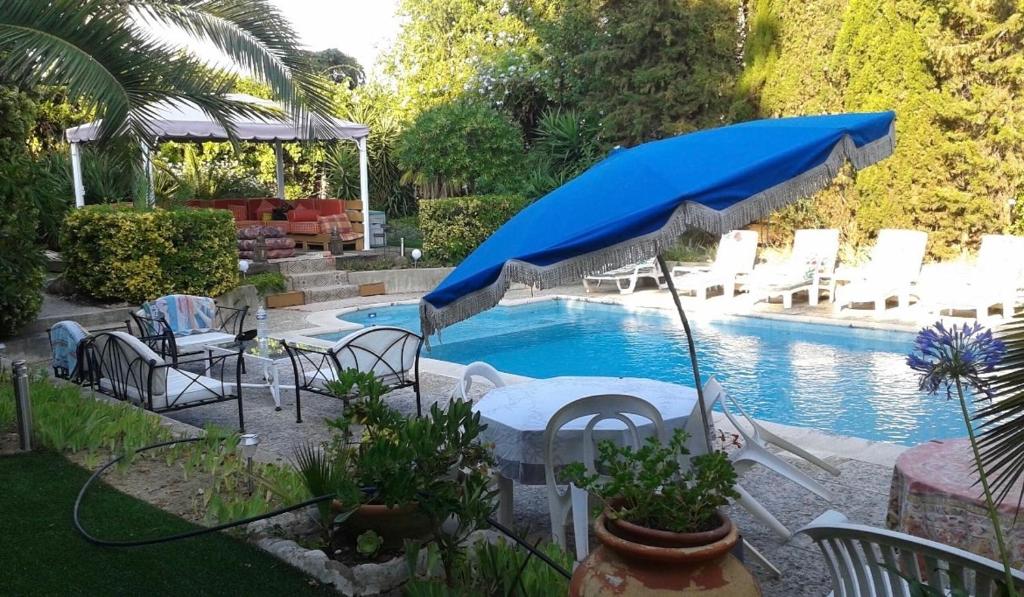 a pool with white chairs and a blue umbrella at Studio indépendant en villa Calme, Jardins et Piscine à 5 min de la Mer in Nice