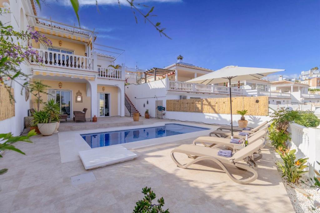 a villa with a swimming pool with chairs and an umbrella at Rd02 La Casa Hermosa in Torrox