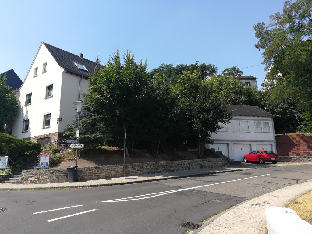 a white house and a red car on a street at Järgen Ferienappartements in Koblenz