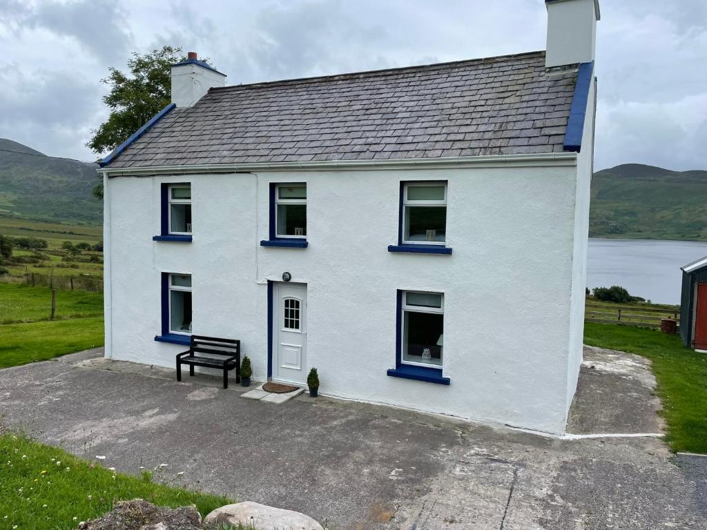 a white house with blue windows and a bench at Padraig cottage in Gortatlea