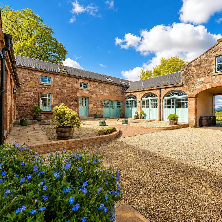 a brick building with blue flowers in a courtyard at Loch Lomond Finnich Cottages in Drymen