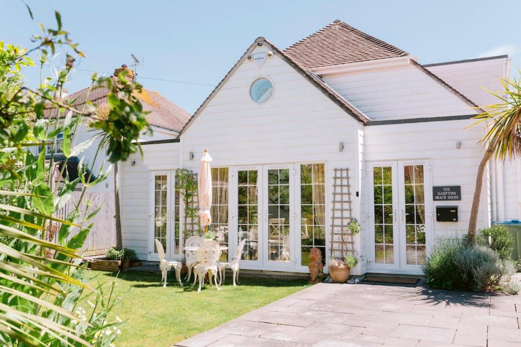 a white house with windows and chairs in the yard at The Hamptons Beach House in East Preston