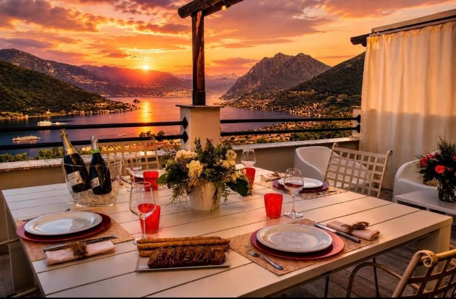 a table with plates and wine glasses on a balcony with a sunset at Lake View 49 in Sale Marasino
