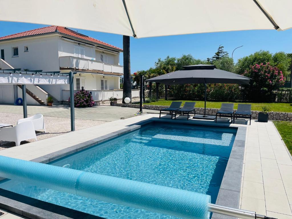 a swimming pool with an umbrella and chairs and a house at Rab Island Apartmets - Palit in Rab