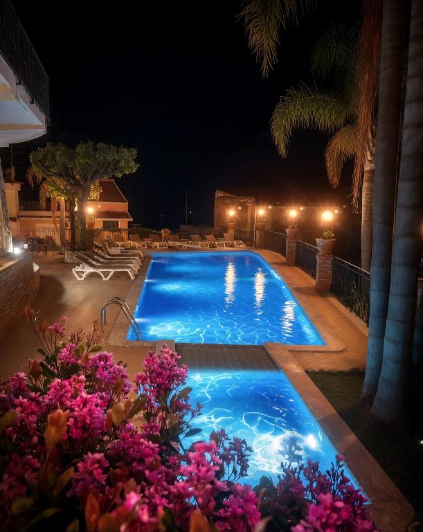 a large swimming pool at night with purple flowers at Hotel Corallo in Taormina