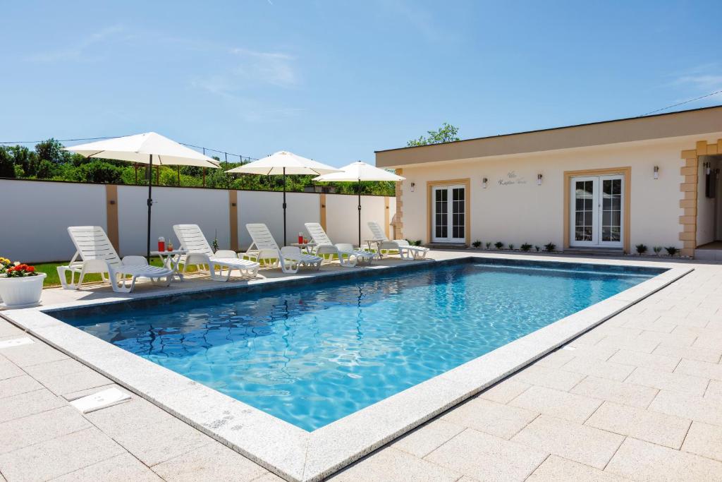 a swimming pool with chairs and umbrellas next to a house at Villa Kaplan Verde in Stolac