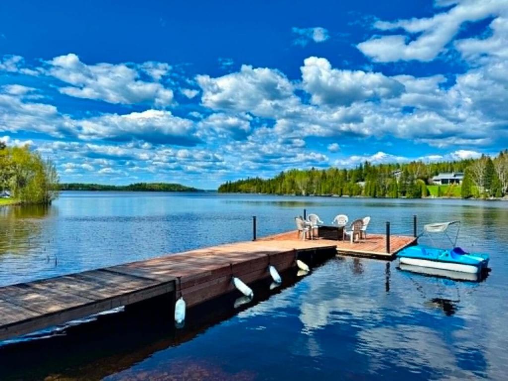 a dock with chairs and a boat on a lake at Chalet au bord du lac à la Baie Boudreault in Alma