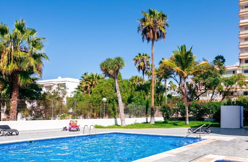 a swimming pool with palm trees and a building at El Delfín in Playa de las Americas