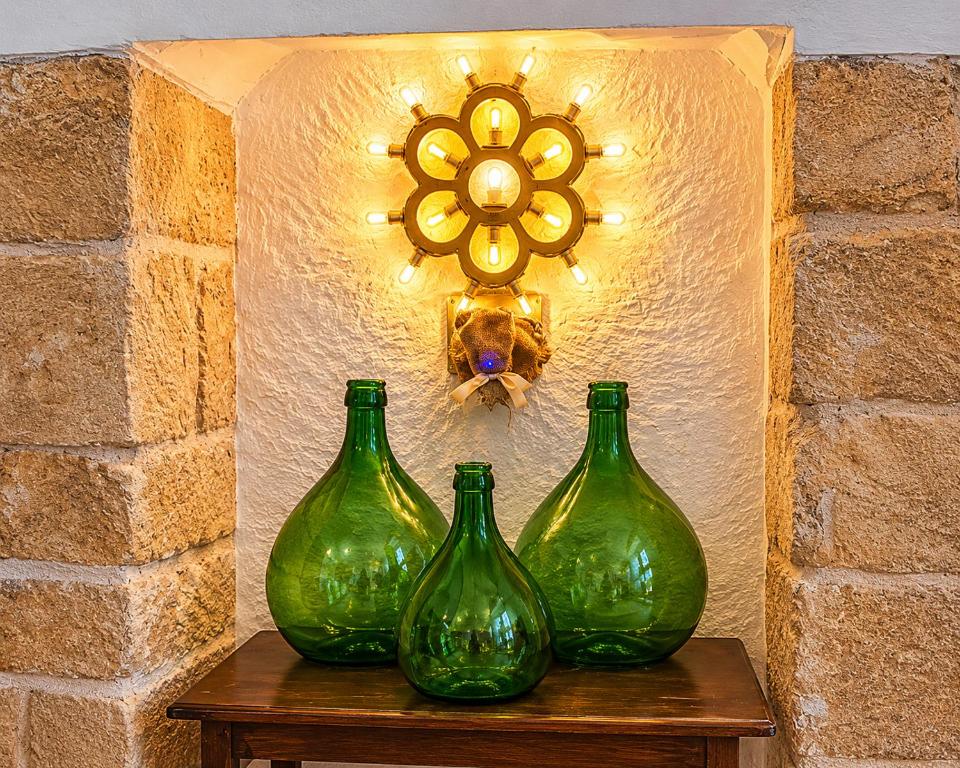 three green glass vases on a table with a light at Ulìa - Stone house tra borgo antico e mare in Giovinazzo