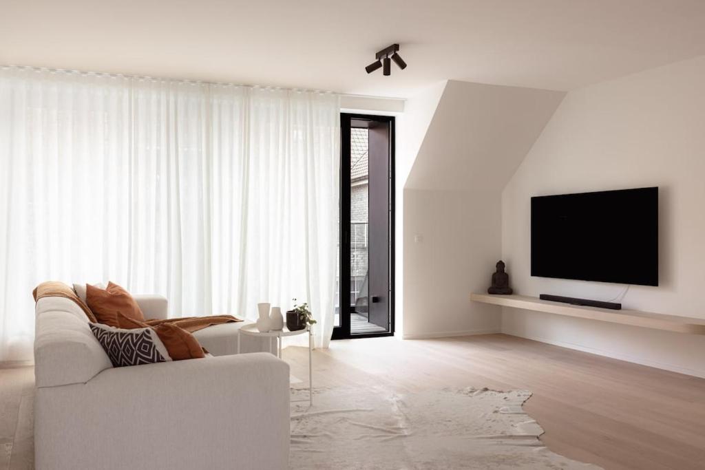a living room with a white couch and a tv at Sunny duplex penthouse, close to beach, parking in Knokke-Heist