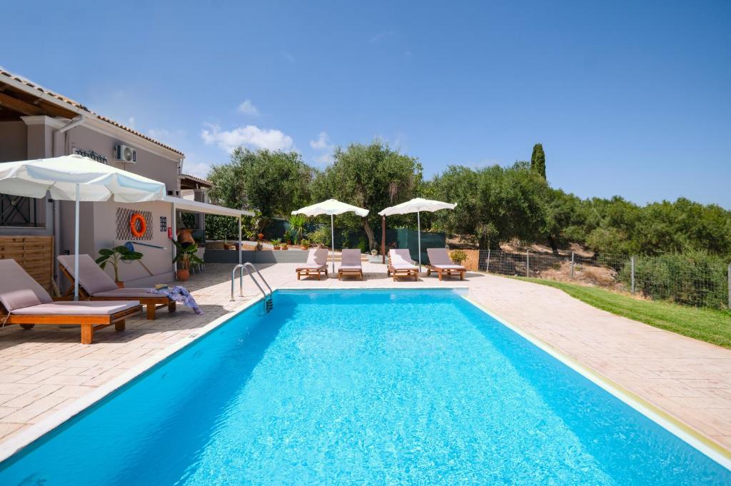 a pool with chairs and umbrellas next to a house at Villa ChrisDina in Nýmfai