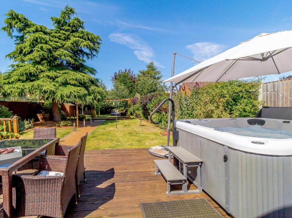 a hot tub on a deck with chairs and an umbrella at 3 Bed in Kings Lynn oc-43259 in Dersingham