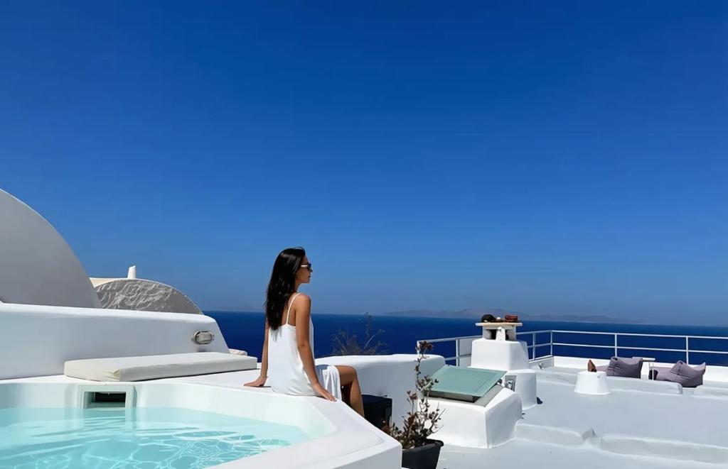 a woman sitting next to a bath tub on the side of a house at OUTOPOIA CAVE STUDIOS in Oia