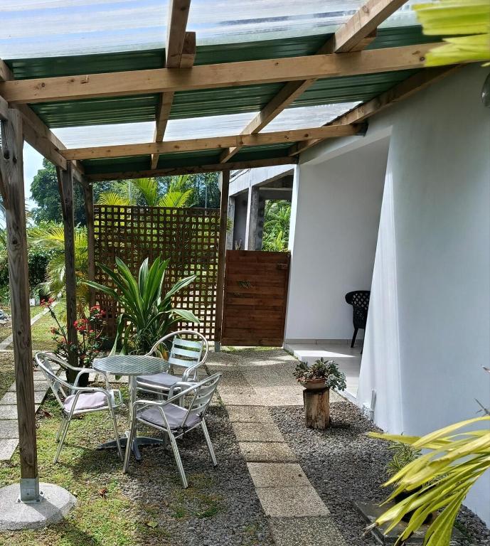 a patio with a table and chairs and a wooden pergola at Le petit coin de campagne in Le Robert